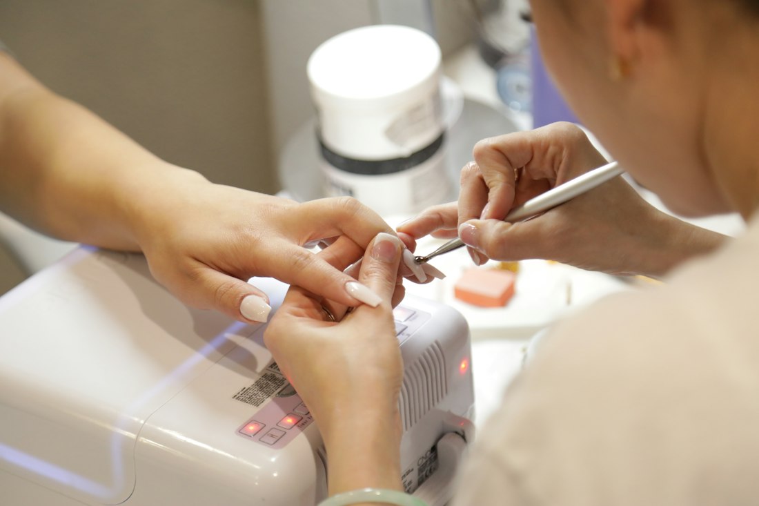 Una manicurista trabaja las uñas de una clienta junto a una lámpara de secado